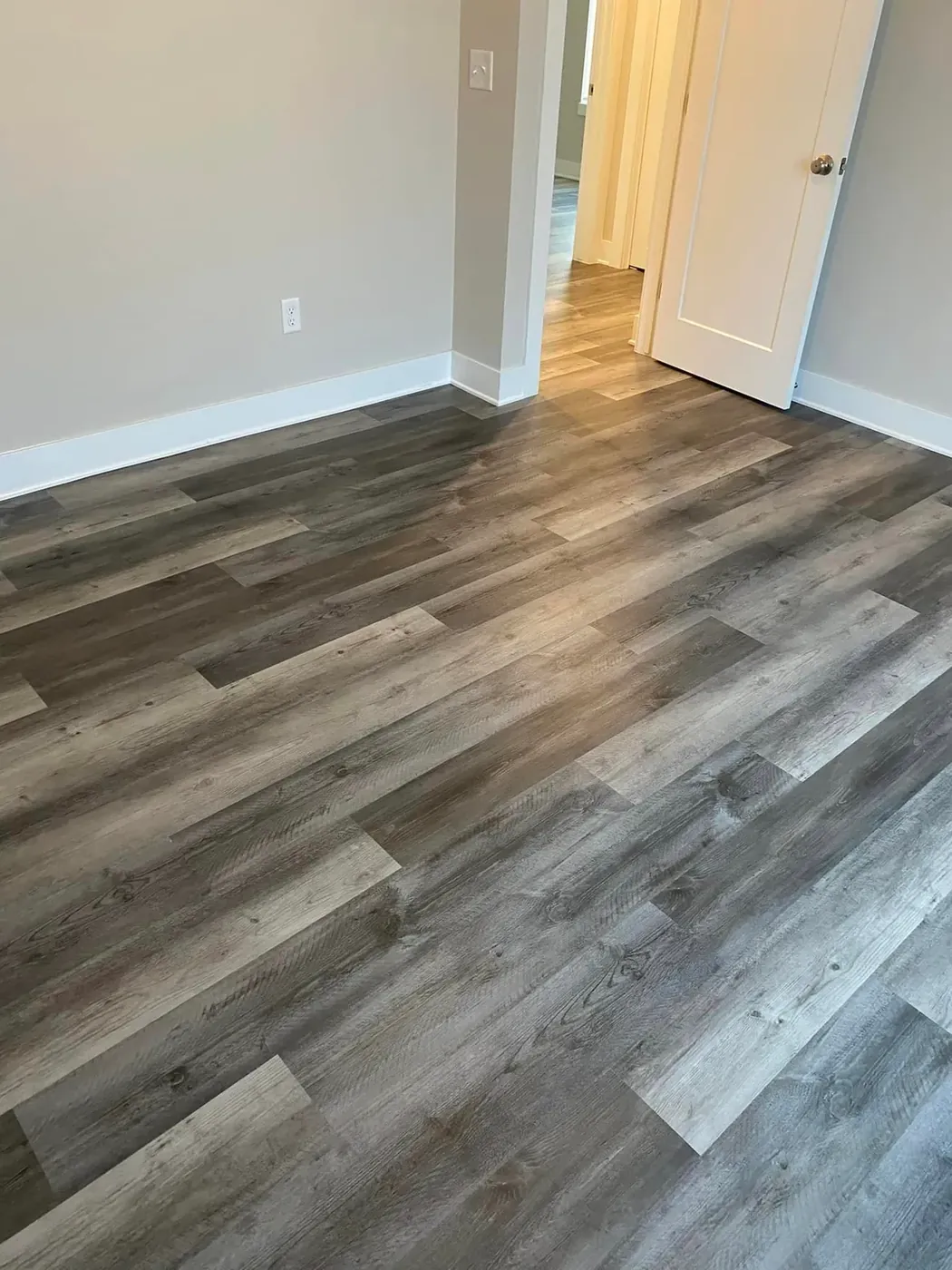 Gray plank flooring running down a hallway to an open door